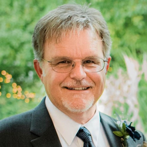 A professional man in a suit and tie, exuding confidence, smiles warmly as he poses for the camera.