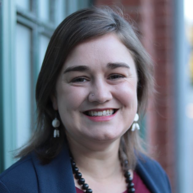 A stylish woman wearing a necklace and a blue blazer, exuding elegance and sophistication.