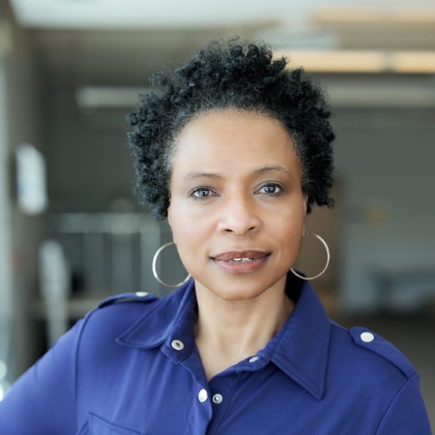 A woman with curly hair wearing a blue shirt, smiling at the camera.
