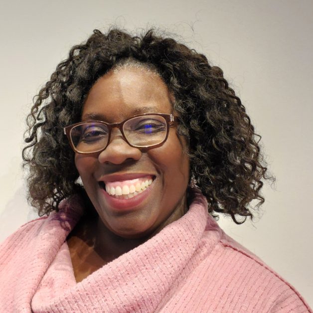 A smiling woman with glasses and a pink sweater.
