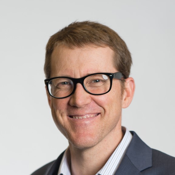 A man in a suit and glasses smiling.